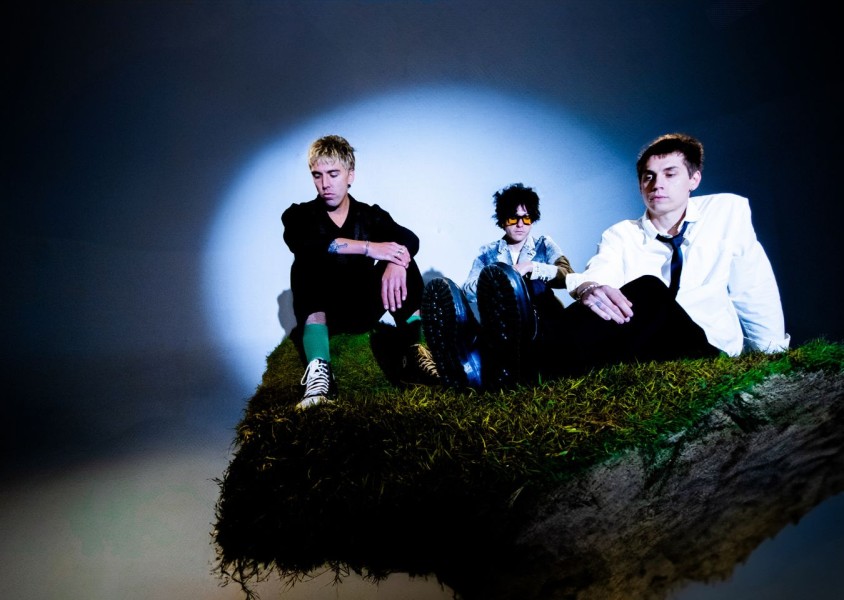 3 men posing on mossy rock with spotlight on themx